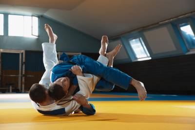 Two young judo caucasian fighters in white and blue kimono with black belts training martial arts in the gym with expression, in action, motion. Practicing fighting skills. Overcoming, reaching target.