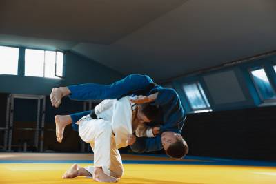 Two young judo caucasian fighters in white and blue kimono with black belts training martial arts in the gym with expression, in action, motion. Practicing fighting skills. Overcoming, reaching target.